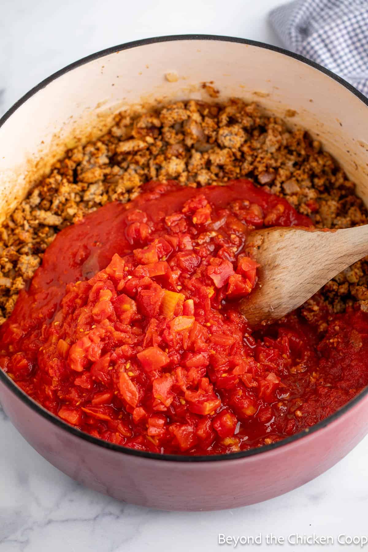 Canned tomatoes in a pot with browned meat. 