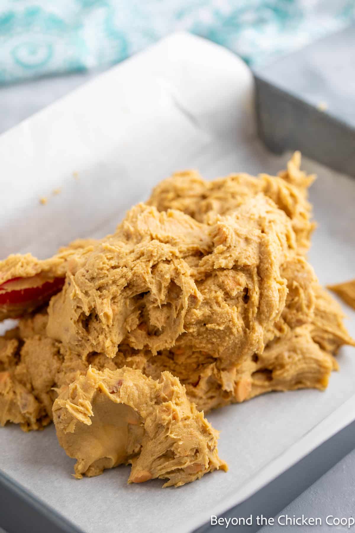 Cookie dough piled into a baking pan lined with parchment paper. 