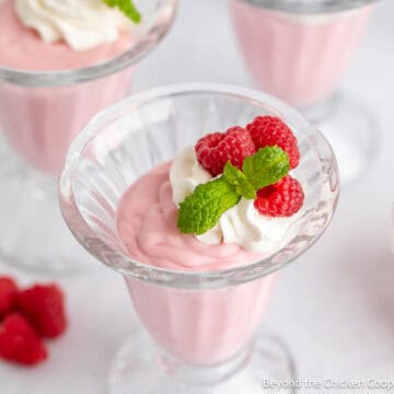 A glass parfait glass filled with raspberry mousse topped with fresh raspberries and whipped cream.