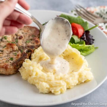 Homemade white gravy being ladled over mashed potatoes.